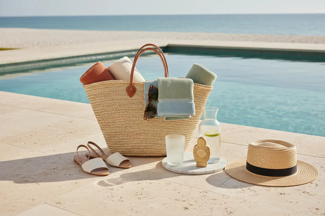 Strandtasche mit Handtüchern, Sonnenbrille, Sandalen und Sonnenhut am Pool